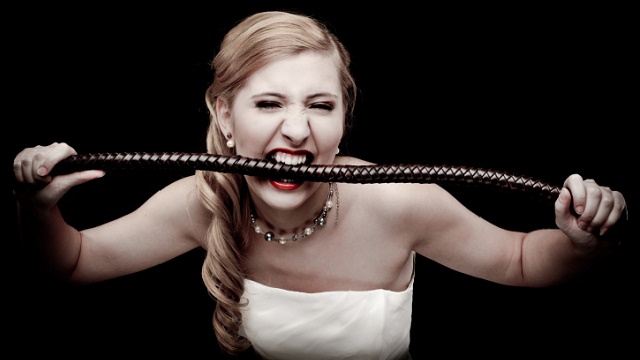A woman bites a whip.