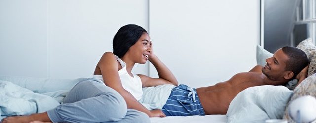 A happy young couple talking together while lying in bed