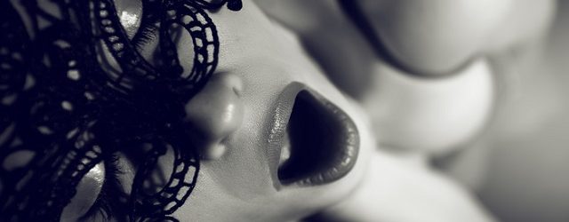 black and white shot of passionate woman with mouth open with orgasmic feeling, covering face with mask, eyes closed.