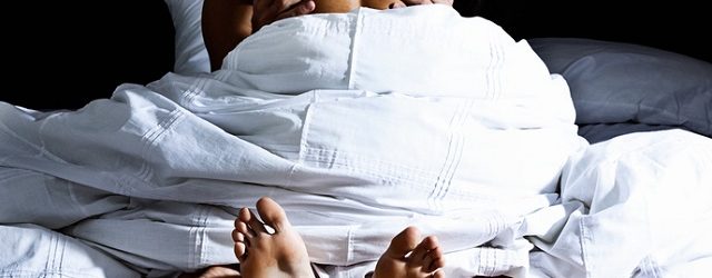 Backview of an anonymous couple making enthusiastic love, the woman on top, under a white duvet.