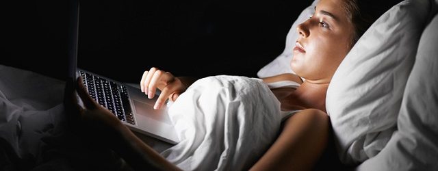 A pretty brunette browsing on her laptop while lying in bed