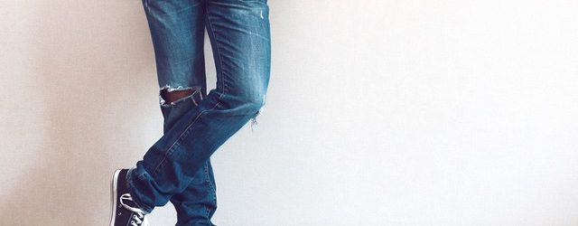 Young fashion man's legs in jeans and sneakers on wooden floor