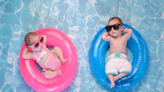 Two babies floating on rings in a pool, one dressed in blue and one in pink
