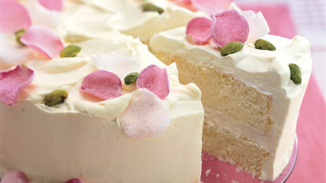 A white cake with white icing, decorated with rose petals
